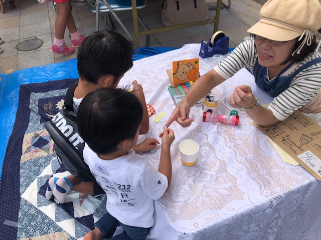 子ども２１のブースの隣は「小野田のわくわくさん」こと尾崎さんが手作りおもちゃとアートバルーンのコーナーを出していました。おなじみ「輪ゴム鉄砲」や「ブーメラン」の他にもたくさんの種類のおもちゃが並んでいました。
子ども達はわくわくさんのおもちゃを手に取って「とんだ！」「すご～い！」と大喜び。