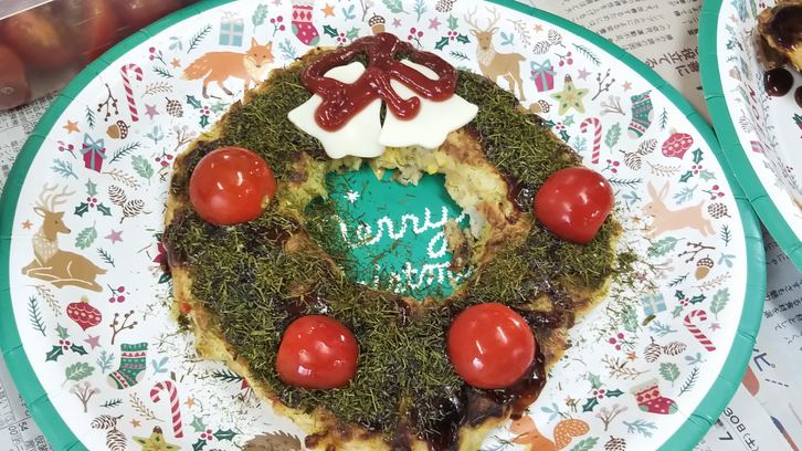 さて一方、西宇部ブロックが準備したお好み焼きは、キャベツの他に里芋、パプリカ、コーン、玉ねぎが入った具だくさん。
大きく丸く焼いたお好み焼きの中心を丸くくりぬいて、ソースをぬってたっぷりの青のりをかけ、チーズやプチトマトで飾り付けると…